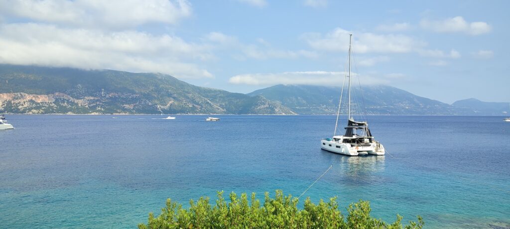 A sleek white luxury catamaran anchored in a crystal-clear turquoise bay in Croatia, surrounded by lush green hills under a bright sky.