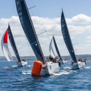 Racing yachts tightly maneuvering around an orange turning mark during a regatta, showcasing tactical boat placement and crew action.